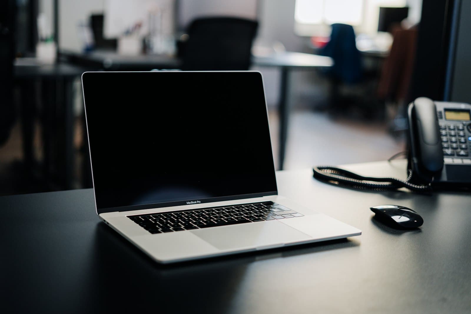 A laptop and a desk phone on an office desk in low light