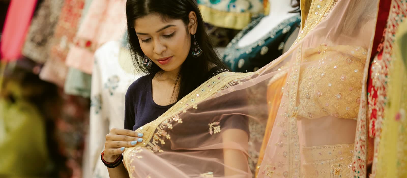 A woman smiling as she looks over an embroidered dupatta in a clothes shop